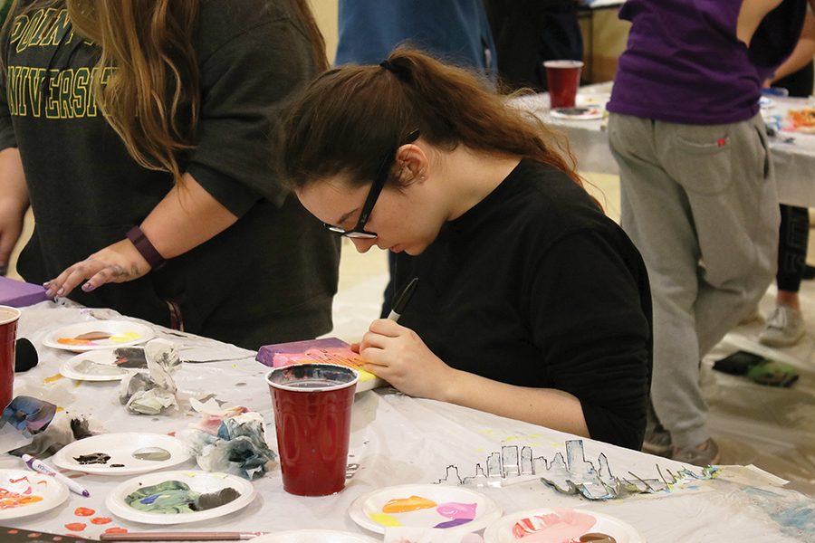 Freshman theater arts major, Sarah Carson, paints at one of the tables in the Lawrence Hall lobby during the “Paint the City” event Thursday night. CAB provided painting supplies along and an outline of the Pittsburgh skyline along with canvases for students to decorate.