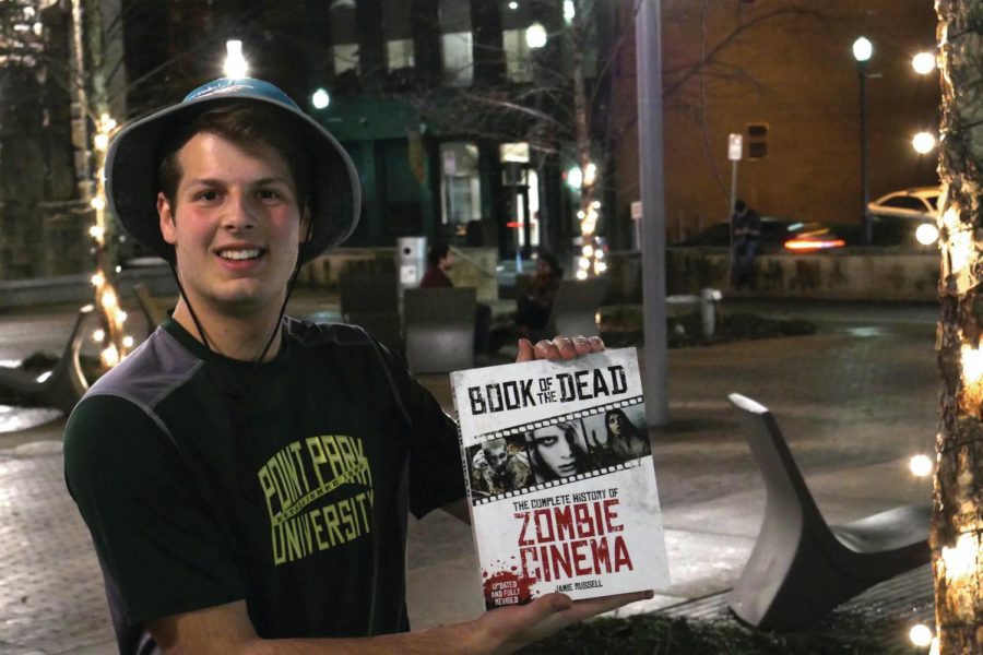 Sophomore Kyle Kuhns poses with the texbook used in the university’s new Zombie Cinema class taught by Matthew Pelfrey.