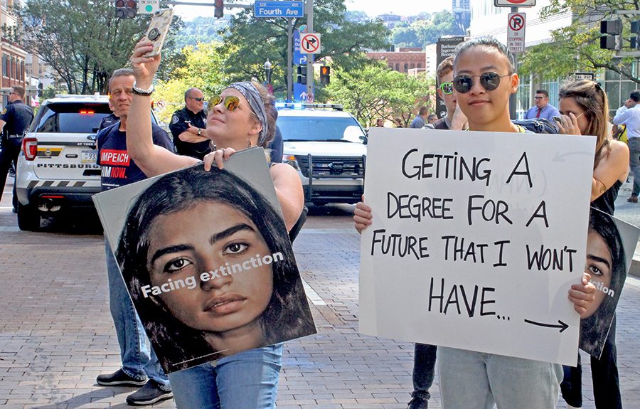 Annie Hanichak, a student at Pitt, holds a sign that reads “Getting a degree for a future that I don’t have. Not pictured is the back of her sign, which reads, “What a waste of money.