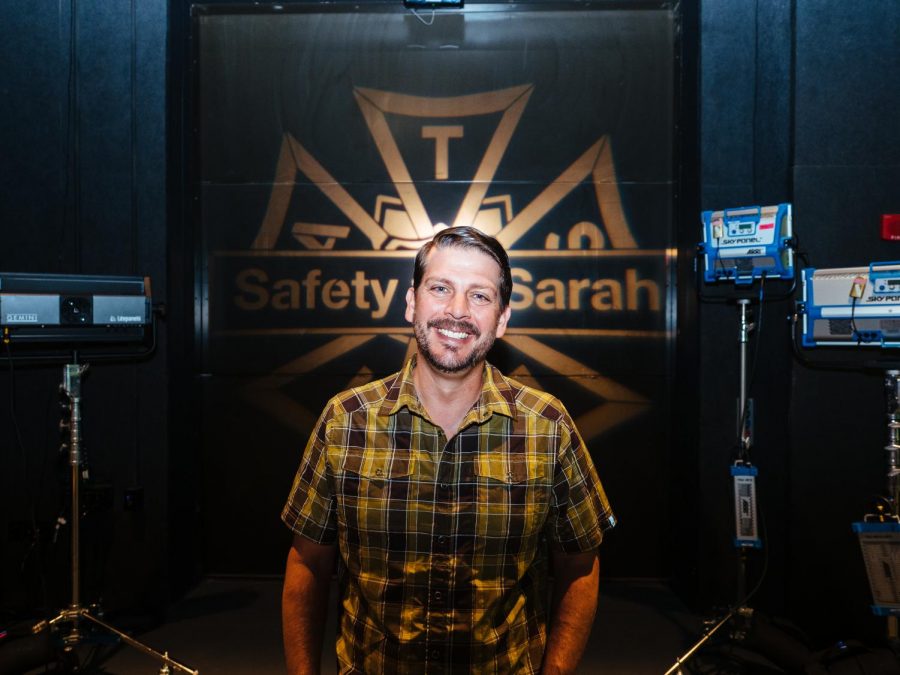 Cinema Safety Coordinator Terry Shirk poses in front of a Safety for Sarah light that shines on a wall in the soundstage of the Playhouse.