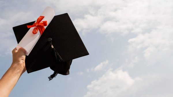 A hand holding a diploma and a graduation cap.