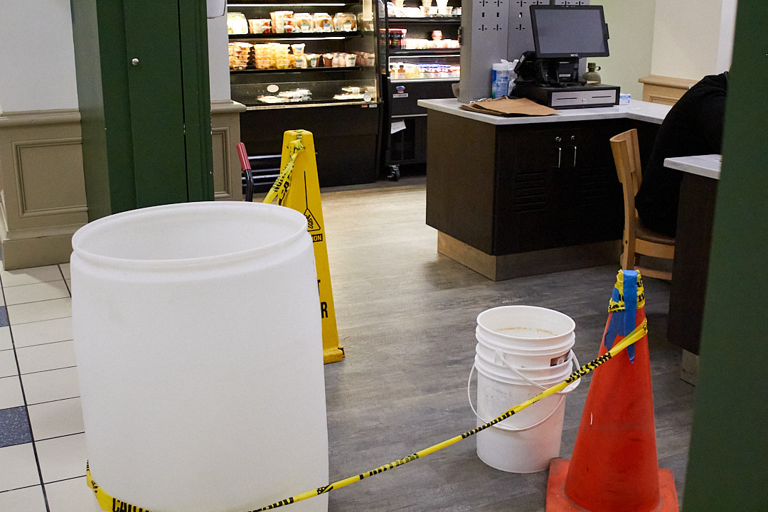 Buckets and barrels sit on the floor catching water droplets from the ceiling of the Point Cafe in Lawrence Hall.