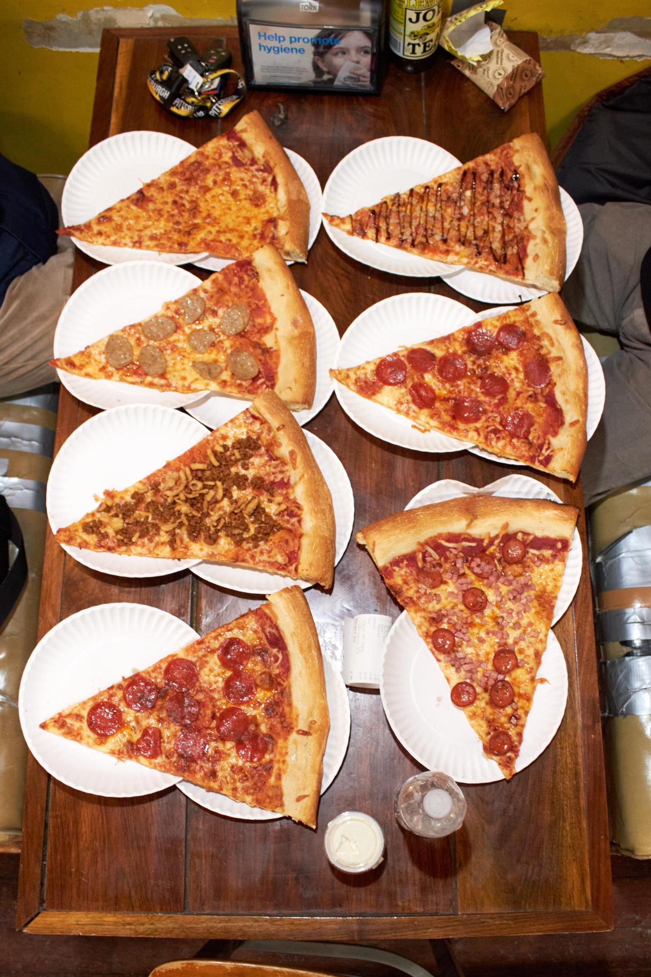 (Top to bottom) A slice of cheese, sliced sausage, chorizo crispy onion, pepperoni, bruschetta, pepperoni and ham with mini pepperoni all sit on a table with ranch and a bottle of Joe's lemon tea at Benny Fierro's Pizza. 